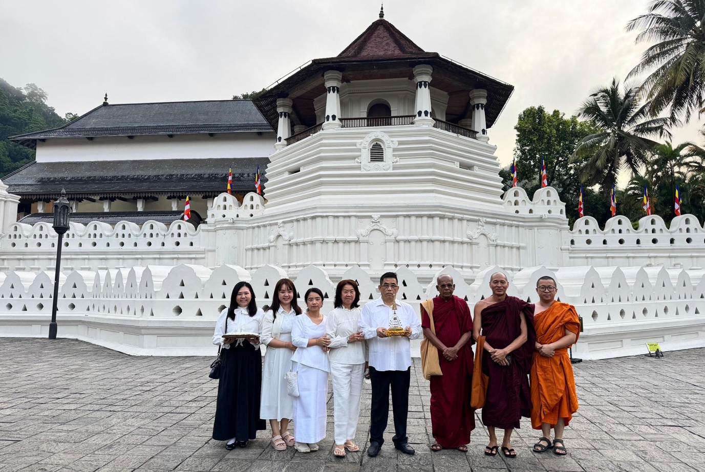 A group of people standing in front of a white buildingDescription automatically generated